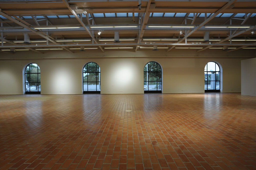 Yleisnäkymä Porin taidemuseon isosta näyttelyhallista. Neljä kaari-ikkunaa, joista on näkymä Kokemänejoelle.