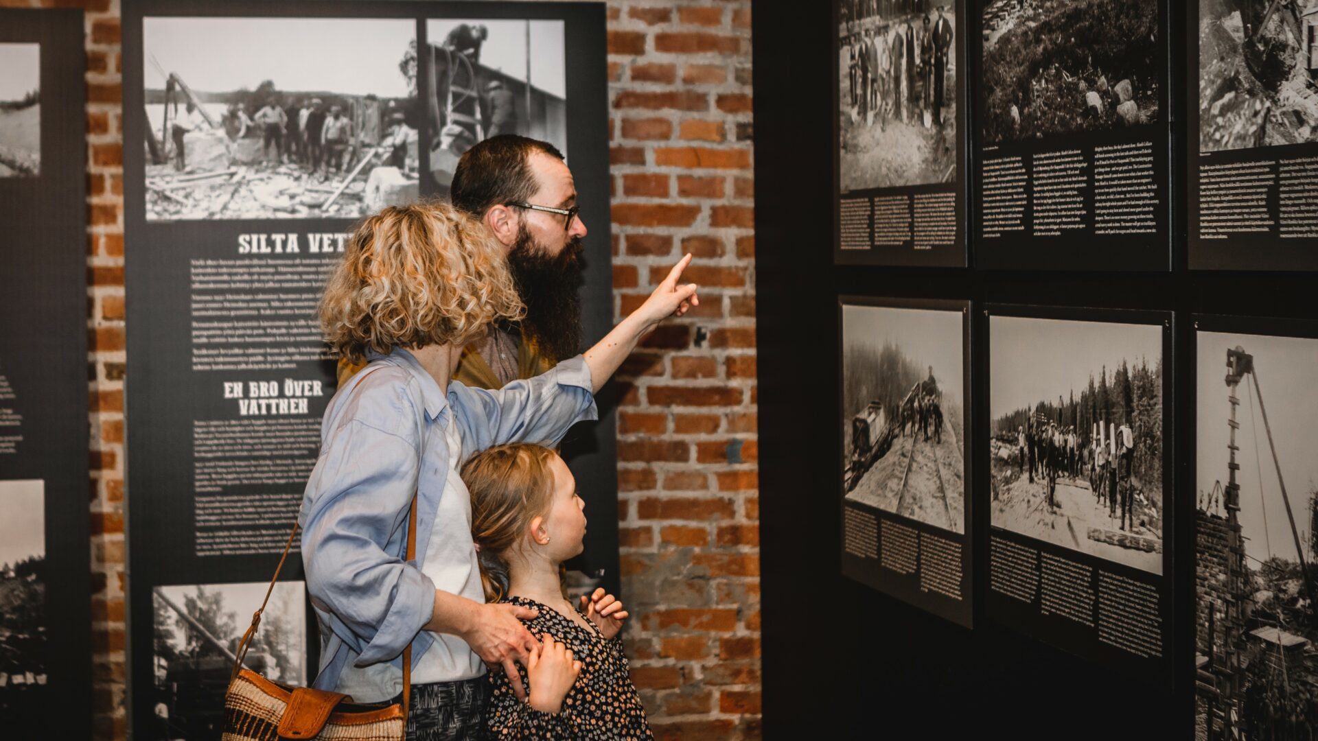 Kuvassa on perhe, nainen, mies ja tyttö tutustumassa museonäyttelyssä valokuviin.