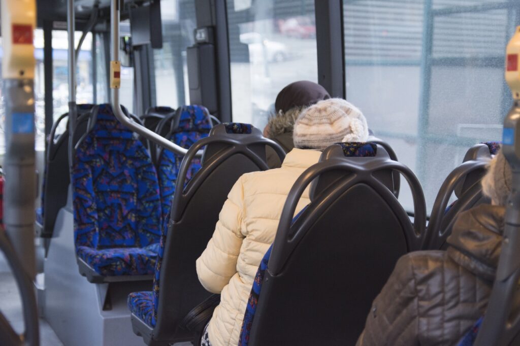 Valkotakkinen henkilö istuu linja-autossa