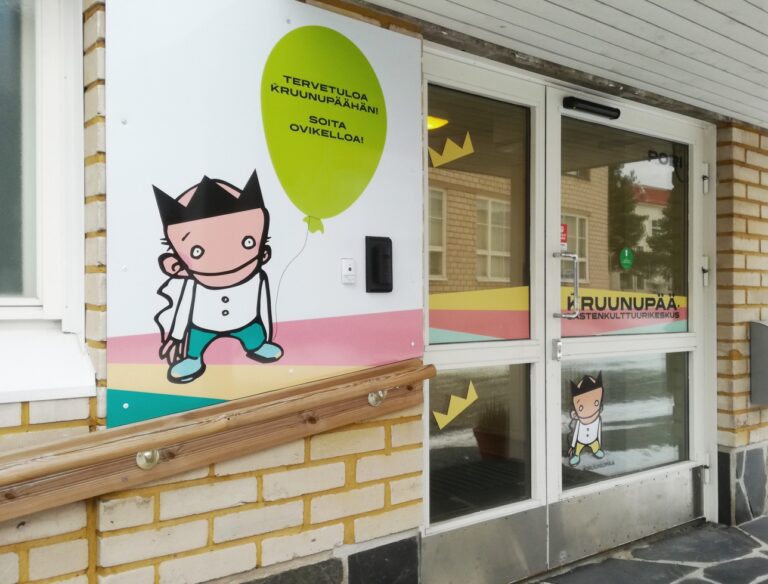 Lastenkulttuurikeskus Kruunupään ulko-ovi, ovessa graafisia teippauksia ja teksti: Soita ovikelloa!