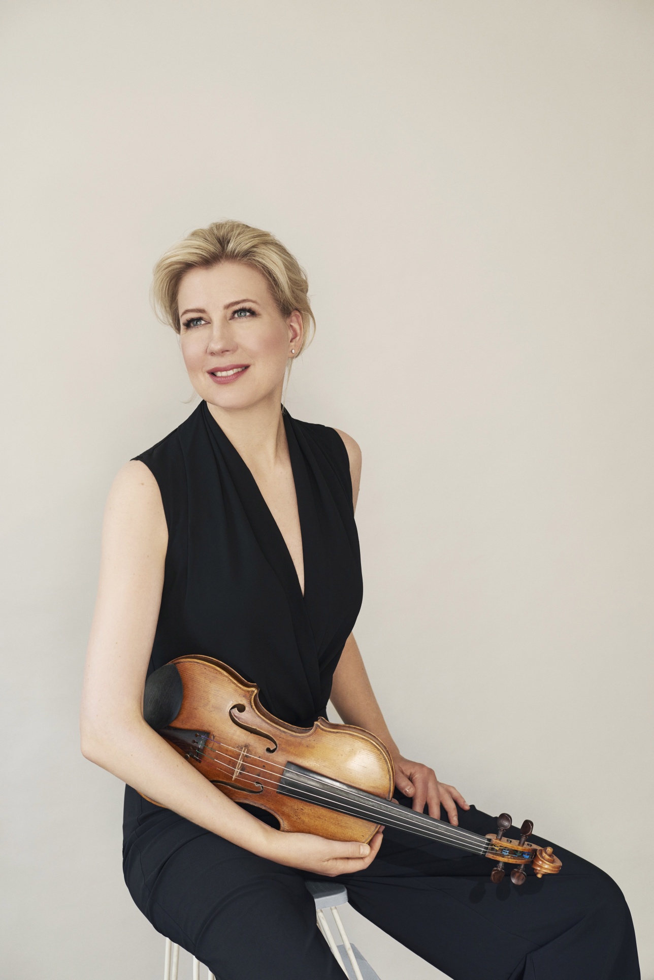 Viulisti Elina Vähälä istuu vaaleaa taustaa vasten mustassa haalariasussa viulu käsissään.
