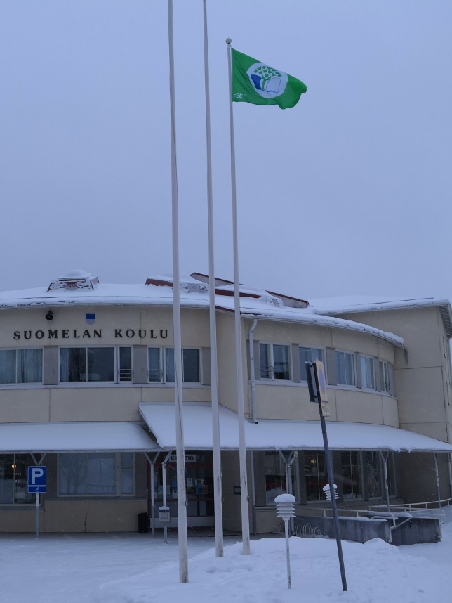 Lavian koulurakennus talvella, edessä vihreä lipput tangossa