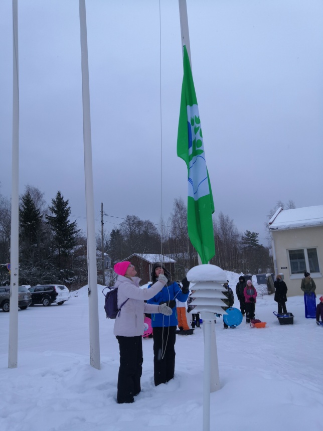 Kaksi lasta nostaa vihreää lippua salkoon talvella 