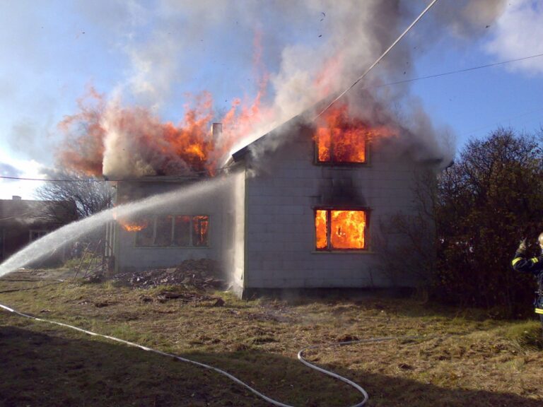 Vanha rakennus täydenpalon vaiheessa. Palomies sammuttaa taloa suihkuputkella.