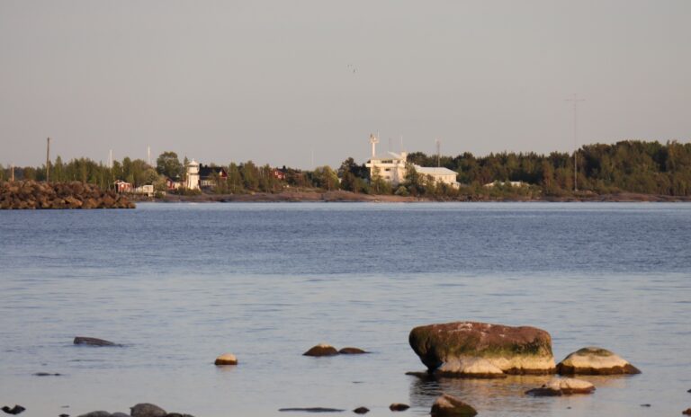 Kallon majakka ja luotsiasema kuvattuna Reposaaren suunnasta. Etualalla Reposaaren takarannan kivikkoinen ranta.