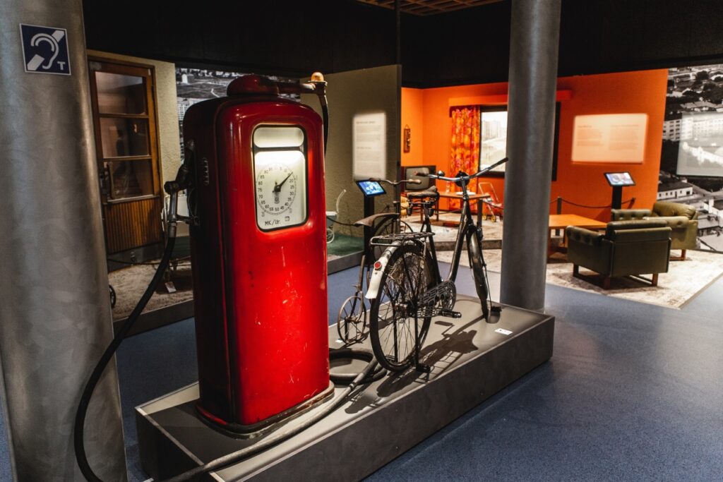 Etualalla punainen bensa-automaatti ja polkupyörä ja takana oranssin värinen huone