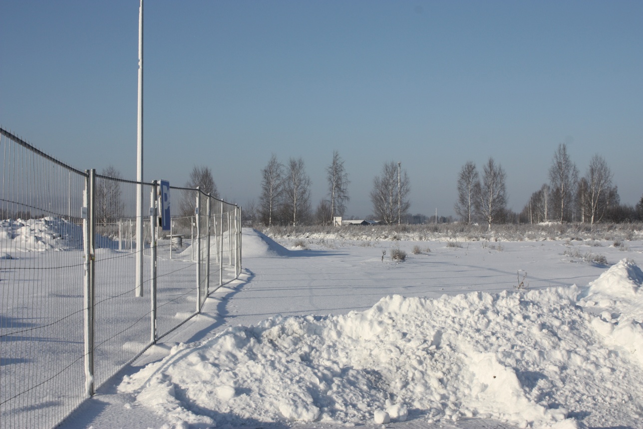 Luminen kuva peltoaukeasta työmaan lähellä, vasemmalla menee aita ja kaukaisuudessa puita 