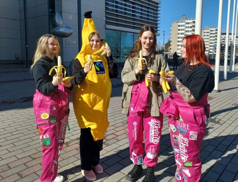Neljä ihmistä vierekkäin ulkona SAMKin edessä, kolmella on pinkit opiskelijahaalarit ja yksi on pukeutunut keltaiseen banaanipukuun.