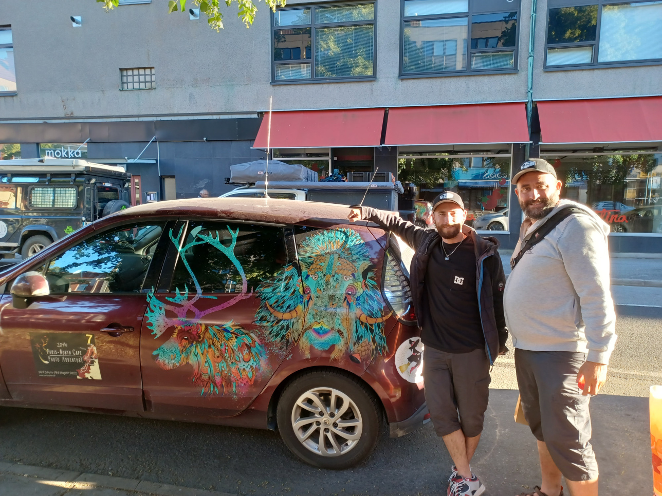 kaksi miestä taiteellisesti maalatun auton edessä 