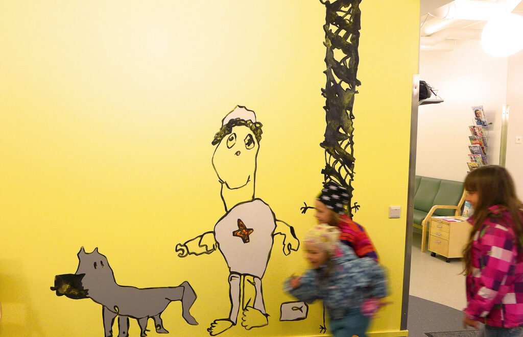 Children run in front of the art on the wall of the child health clinic.