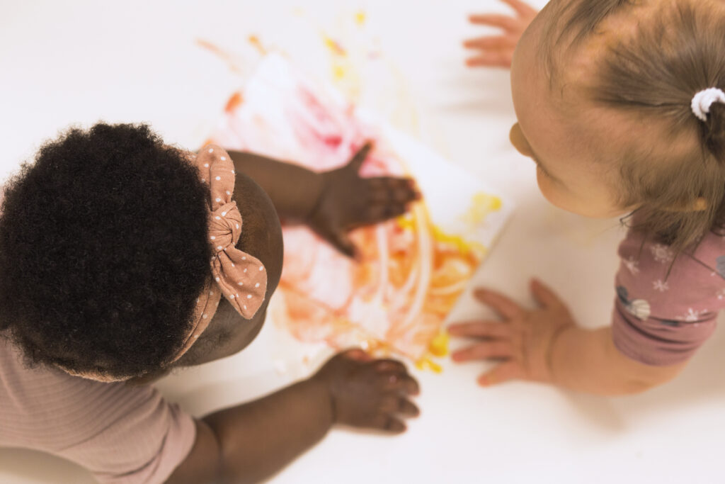 Two babies are painting with their hands and interacting.