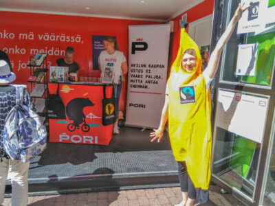 banaanipukuinen ihminen Pori-julisteiden edessä hymyilemässä