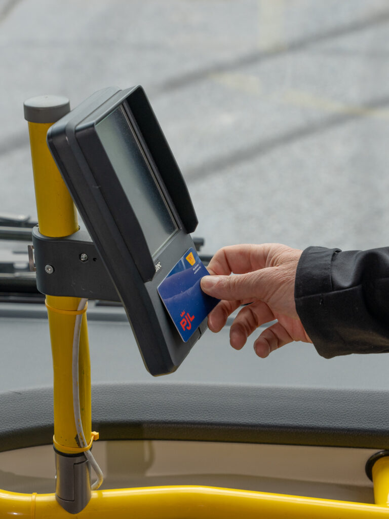Käsi ojentamassa maksukortti linja-auton kortinlukijaan