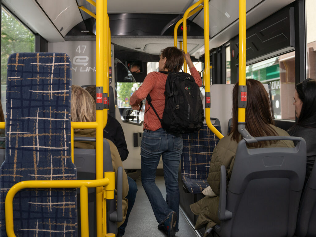 matkustajia bussissa, yksi matkustaja seisoo käytävällä reppu selässä