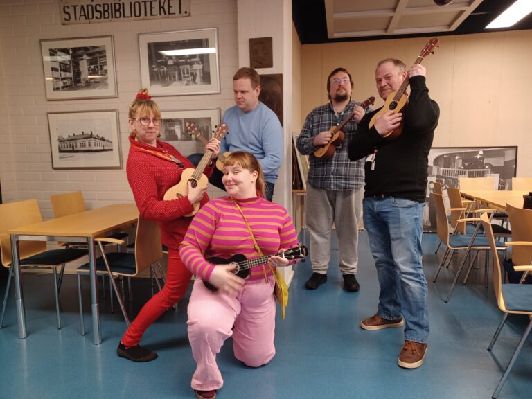 Viisi henkilöä poseeraa ukulelejen kanssa