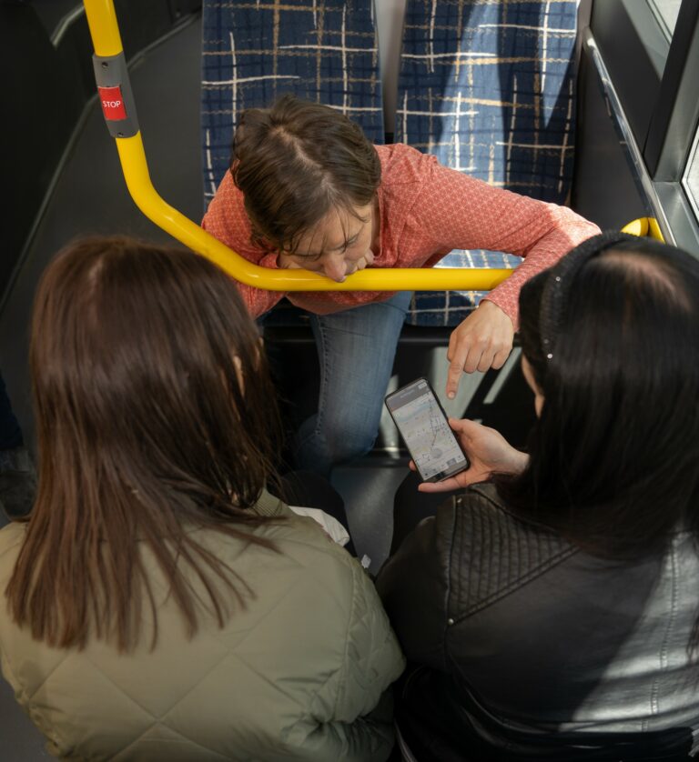 Kolme henkilöä istuu bussissa ja tutkii puhelimen näyttöä