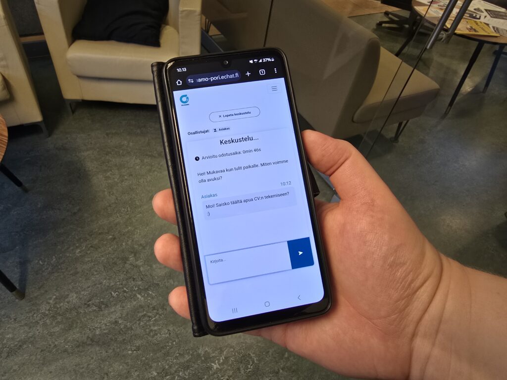 Kuva, jossa puhelin henkilön kädessä. Näytöllä näkyy Ohjaamon chat.