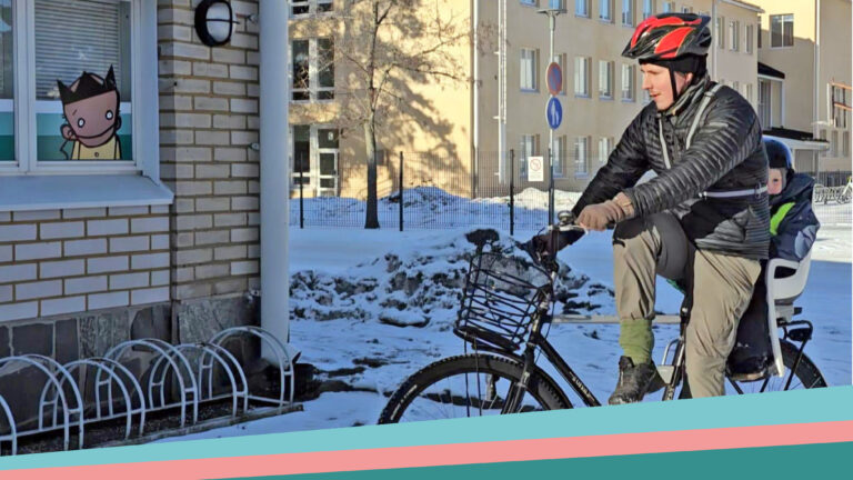 Aikuinen pyöräilee Kruunupään pyöräparkkia kohti takahäksällään lapsi.