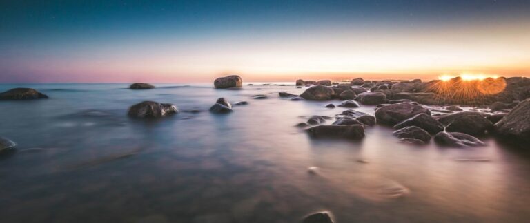 Auringonlasku, meri, valot ja kivikkoa