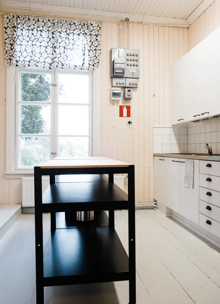 vaalea keittiö, tumma puinen pöytä keskellä huonetta, valkoiset kaapistot, seinustalla ikkuna ja sähkökaappi