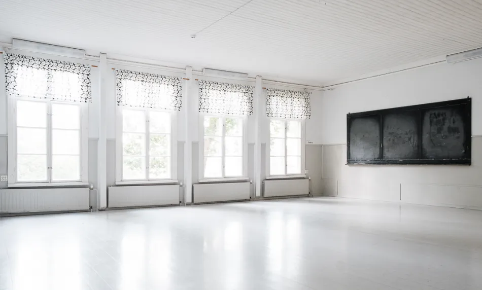 juhlasali, jossa valkoinen lattia, neljä isoa ikkunaa joissa verhot, seinällä tumma taulu