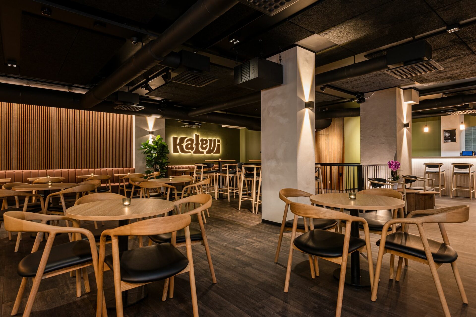 Kalevi Bar & Kitchenin yläkerran sali tyhjillään puunvärisine pöytineen ja taustalla seinällä Kalevin valaistu logo.
