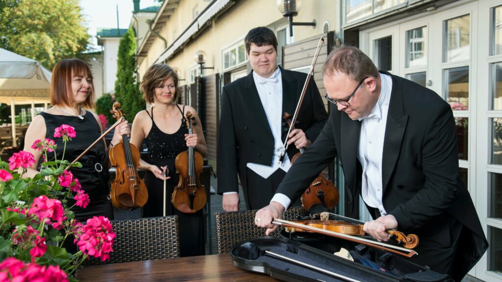 Pori Sinfoniettan II viulistit Beata Sibielak, Anna Hoffström ja Hokto Sorsa katsovat, kun Stefan Kavén asettaa viulua koteloon kesäisellä terassilla.